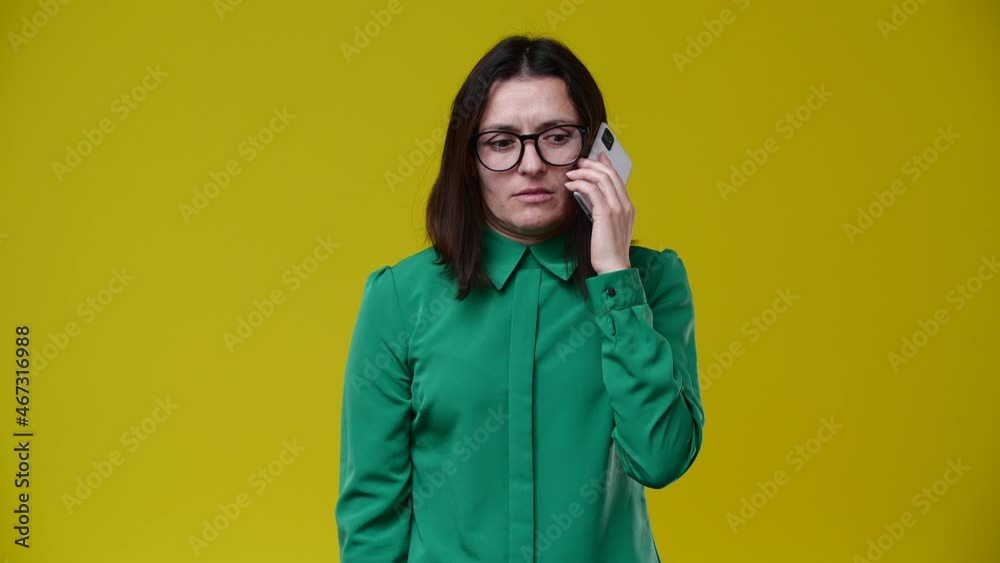 the woman received a call and was told unpleasant news, she became very passive and angry, she says no, she is brunette, short-haired, wears glasses, is wearing a green shirt, the background is yellow the woman received a call and was told unpleasant news, she became very passive and angry, she says no, she is brunette, short-haired, wears glasses, is wearing a green shirt, the background is yellow