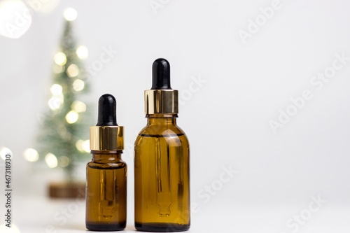 Glass brown cosmetic jar with a pipette on a white background. A bag with presents. Spruce or pine branch. Place for your text. Lights and bokeh. New Year's and Christmas.