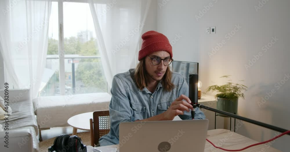 Caucasian male recording podcast in living room using laptop and microphone 
