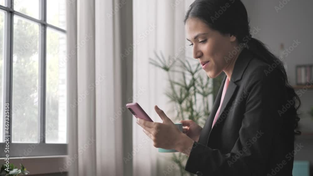Elegant business woman using smart phone mobile by the window indoors,happy young latina businesswoman holding smartphone browsing online checking emails smiling