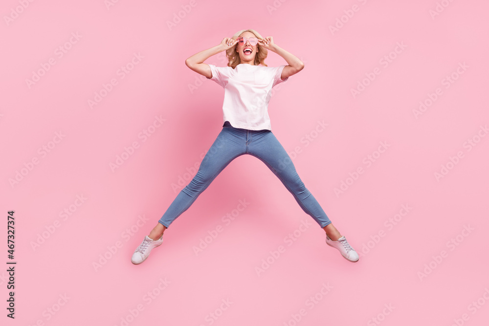 Full body photo of funny young blond lady jump wear spectacles t-shirt jeans sneakers isolated on pink background