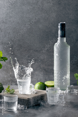 Photo Bottle of vodka with splash shot glass on concrete background with copyspace