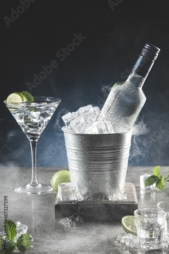 Fototapeta Bottle of ice cold vodka in bucket of ice and glasses on dark background with copyspace