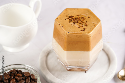 glass with trendy korean beverage dalgona coffee latte - whipped instant coffee, sugar and hot water and milk layers on a marble board, white surface