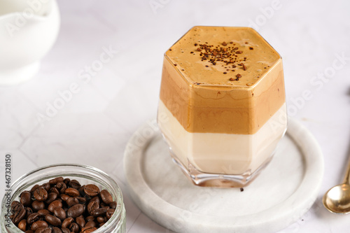 glass with trendy korean beverage dalgona coffee latte - whipped instant coffee, sugar and hot water and milk layers on a marble board, white surface
