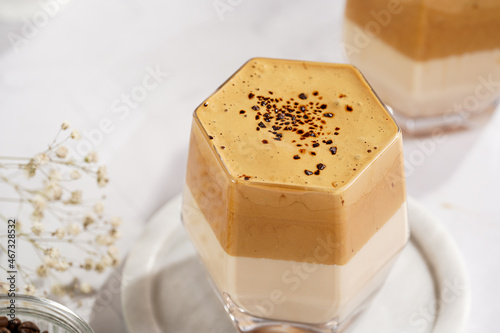 Two glasses with trendy korean beverage dalgona coffee latte - whipped instant coffee, sugar and hot water and milk layers on a marble board, white surface