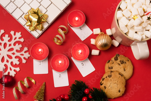 Fototapeta Naklejka Na Ścianę i Meble -  Christmas Home Office and Advent Candles Desk with White Keyboard Christmas Golden Ornaments Cup of Cocoa with Marshmallw and Candy Cane Cookies and Red Candles Red Background Top View