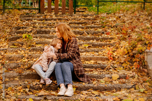 mother and daughter sit and hug on the stairs in the autumn park. 