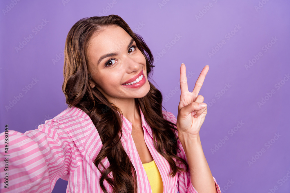 Photo portrait woman smiling happy in casual clothes taking selfie showing v-sign isolated pastel purple color background Photo portrait woman smiling happy in casual clothes taking selfie showing v-sign isolated pastel purple color background
