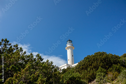 White lighthouse tall tower in greenery on a bright clear blue sky in Greece, Ionian sea. Scenic travel destination. Lefkada island