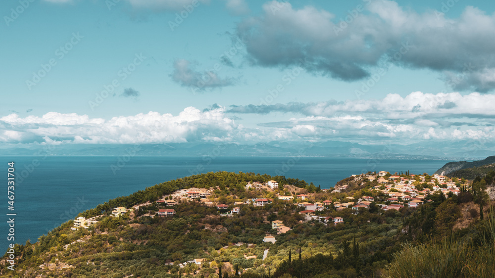 Color graded panoramic traditional greek village with orange tiled roofs on green hills near blue sea shore on Lefkada island, Greece. Travel Europe in summer