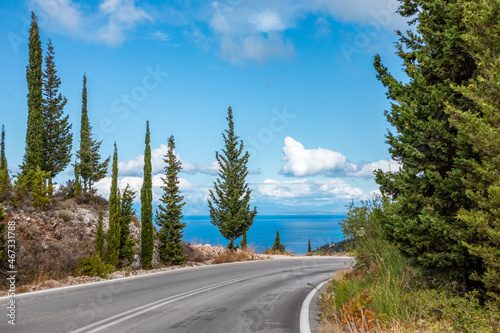 Driving asphalt road right turn with green pine trees and blue vivid skyscape. Travel Lefkada island sea coast, Greece. Scenic day trip by car
