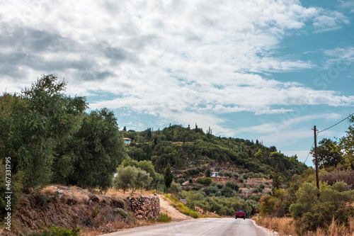 Scenic road to traditional Greek village with scenic cloudscape on green hills on Lefkada island, Greece. Travel Europe in summer by car