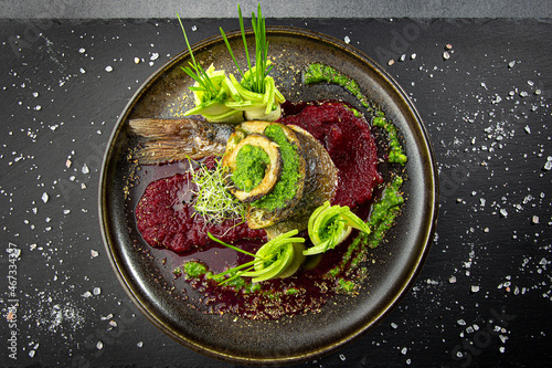 Decorated fish roll with sliced zucchini and red beet puree garnish on dark restaurant dish. Original presentation