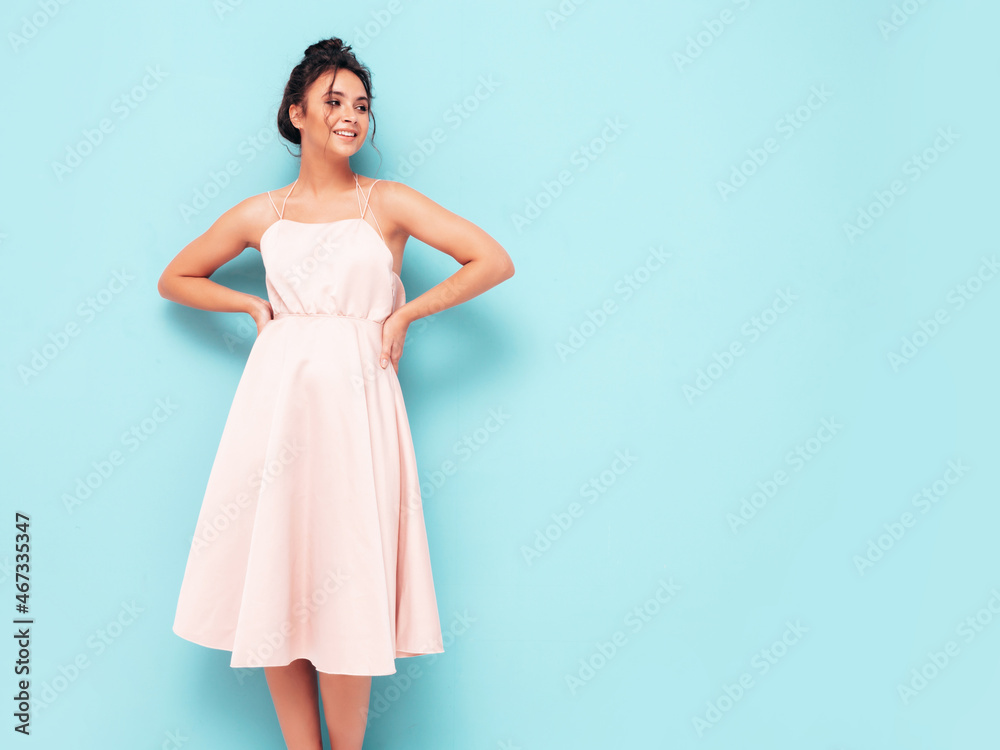 Naklejka premium Portrait of young beautiful smiling female in trendy summer dress. Sexy carefree woman posing near blue wall in studio. Positive model having fun indoors. Cheerful and happy
