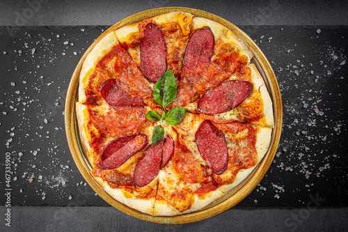 Italian salami pizza with cheese sauce and crispy pepper with roasted spice mix, wooden dish plate on a stone table top.