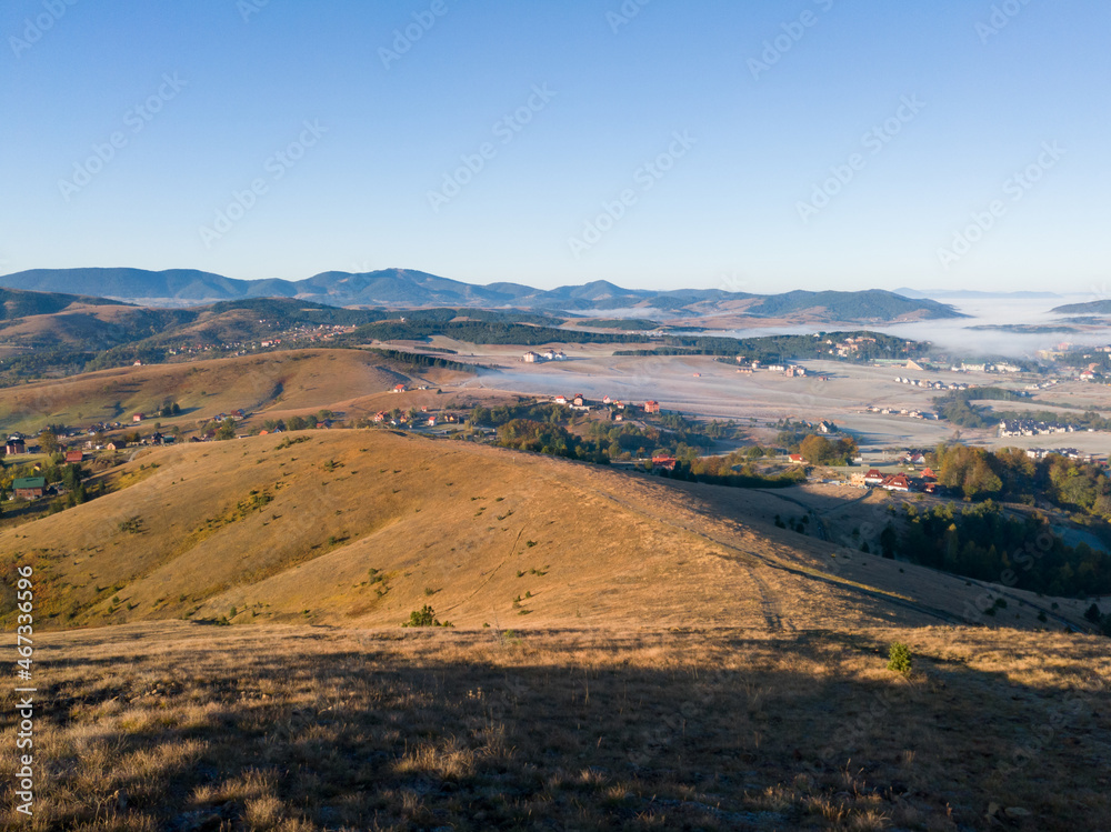 Landscape of the Zlatibor mountain with grassy pastures, hills and part of the tourist town of Zlatibor during the morning in autumn