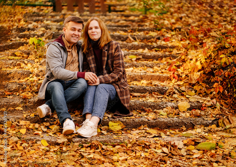 a middle-aged man and woman sit on steps in an autumn park.