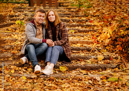 a middle-aged man and woman sit on steps in an autumn park.