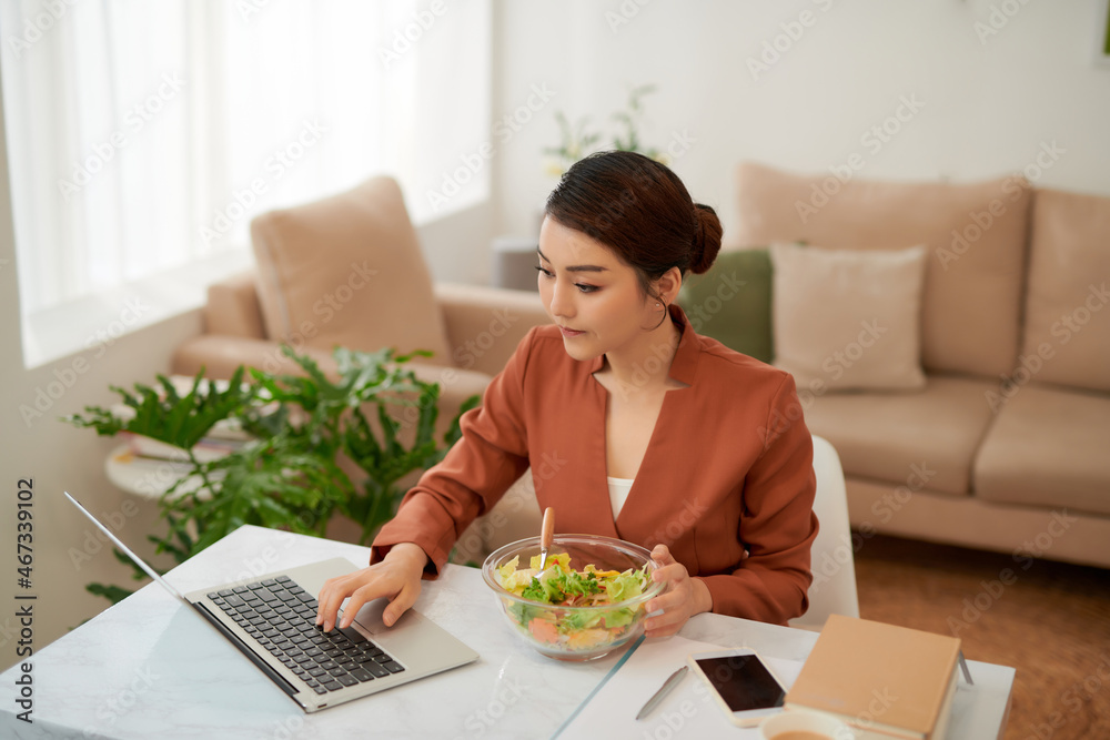 Woman having lunch from glass bowl and using laptop. Woman having lunch from glass bowl and using laptop.