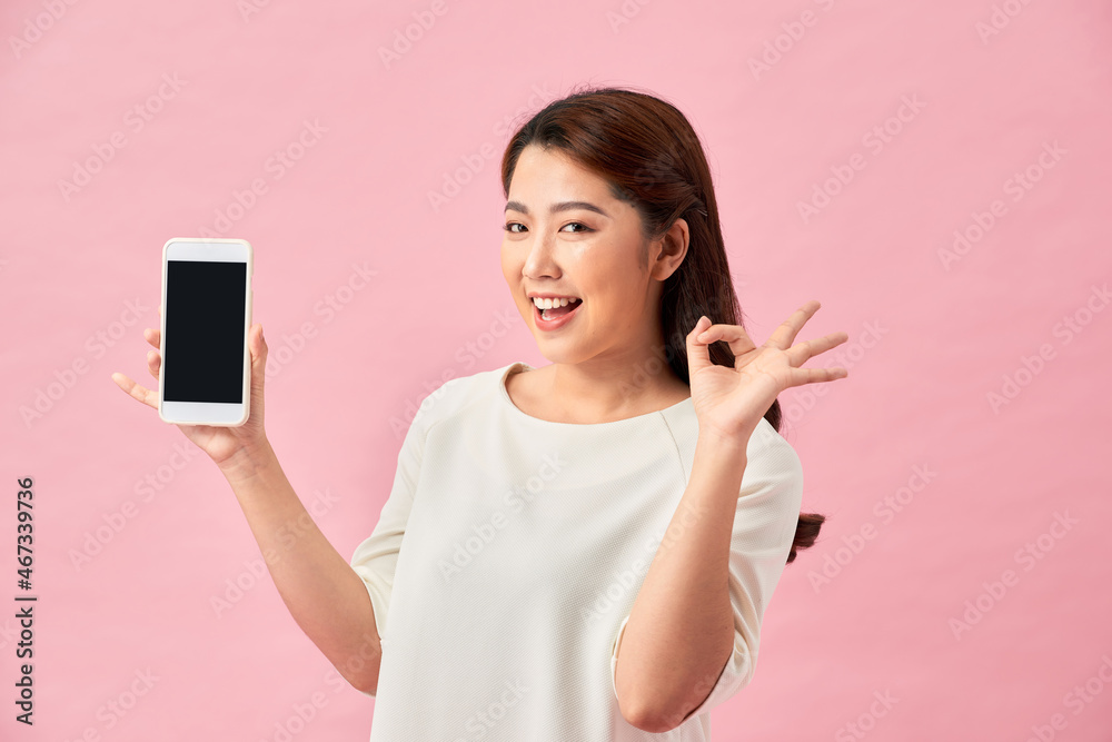 Happy Asian portrait beautiful cute young woman excited holding mobile phone and gesturing ok sign, studio shot isolated on pink background