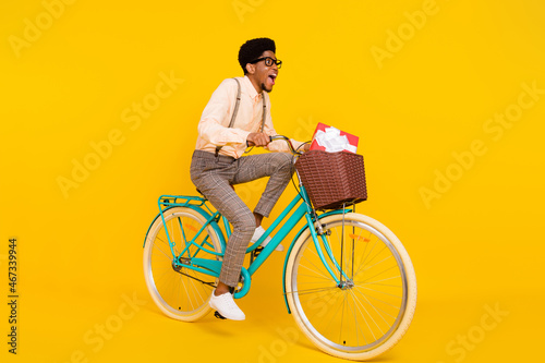 Full length body size photo man riding bike with basket having present isolated vivid yellow color background