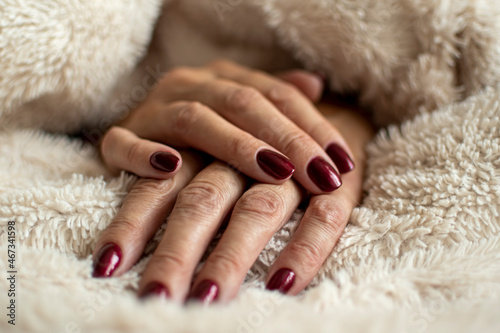 Wrinkled hand skin closeup. Dark red royal nail gel polish, female manicure, beauty treatment in a salon. Selective focus on the details, blurred background.
