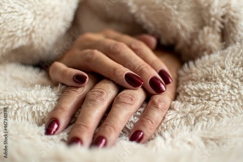 Wrinkled hand skin closeup. Dark red royal nail gel polish, female manicure, beauty treatment in a salon. Selective focus on the details, blurred background.
