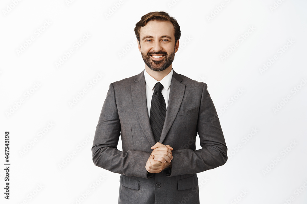 Smiling corporate man working with client, holding hands together, real professional pose, listening to customer, standing in suit over white background Smiling corporate man working with client, holding hands together, real professional pose, listening to customer, standing in suit over white background