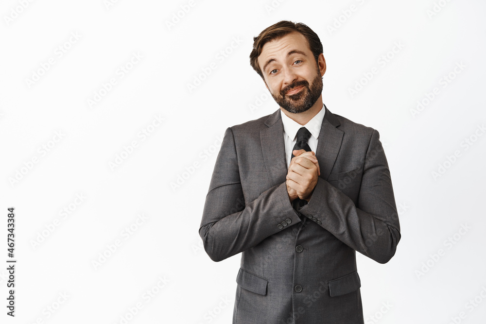 Portrait of pleased and touched businessman, holding hands clenched, looking with grateful, delighted face expression, standing in suit over white background Portrait of pleased and touched businessman, holding hands clenched, looking with grateful, delighted face expression, standing in suit over white background