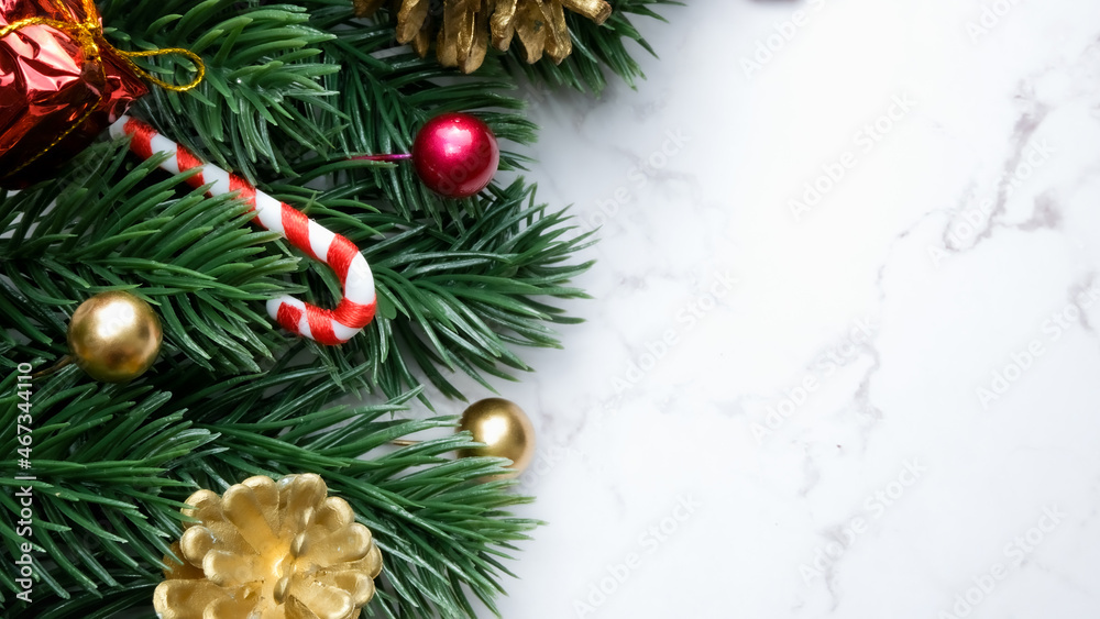 Green pine tree leaves, red christmas decorations and candy canes on white marble background, christmas decorations in bright red color. Simple and creative christmas concept.