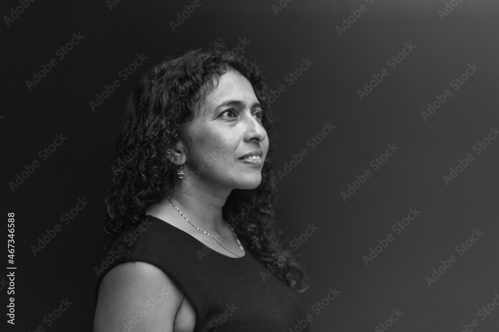 Portrait of Latin woman with wavy hair wearing black clothes, look to side and dark background Portrait of Latin woman with wavy hair wearing black clothes, look to side and dark background