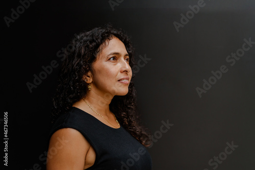 Portrait of Latin woman with wavy hair wearing black clothes, look to side and dark background