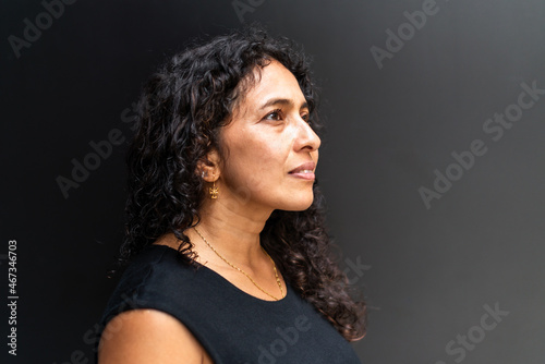 Portrait of Latin woman with wavy hair wearing black clothes, look to side and dark background