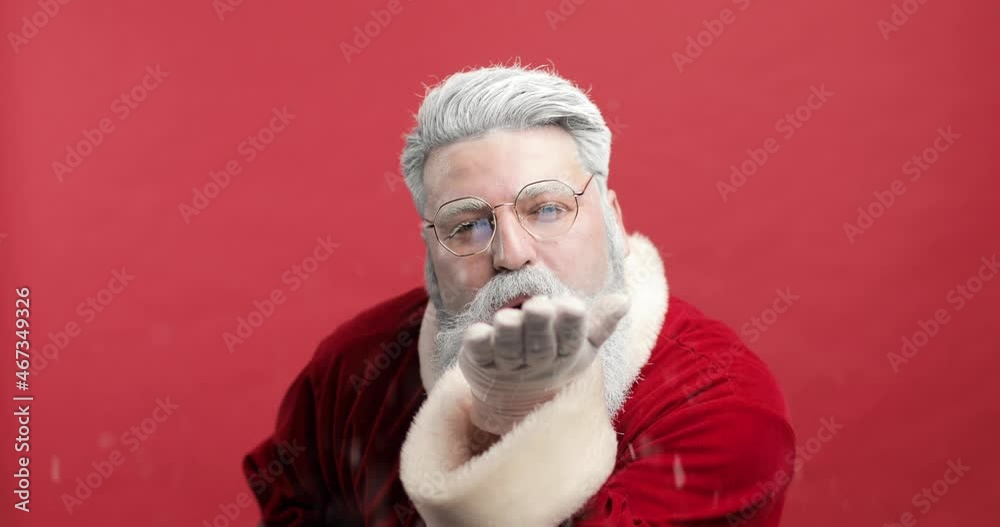 stylish, cheerful, joyful, happy Bearded man in Santa Claus clothing smiling and blowing snow into camera, isolated over red background - christmas concept close up stylish, cheerful, joyful, happy Bearded man in Santa Claus clothing smiling and blowing snow into camera, isolated over red background - christmas concept close up