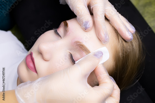 the girl model at the eyebrow lamination procedure  the master erases the remnants of their laminating compositions with a cotton sponge