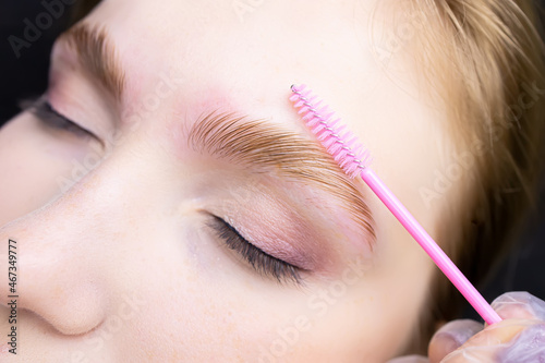 a close-up of the eyebrows on which lamination is performed and the master combs with a brush directing the growth of eyebrow hair