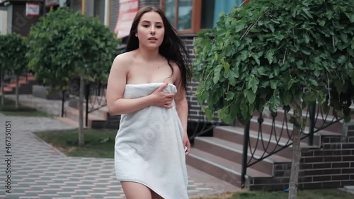 Attractive girl wrapped in bath towel walks along a city street. Glamorous lifestyle. Fashion shot. Charming young woman is relaxing in spa hotel. New day concept. spa resort. slow motion.
