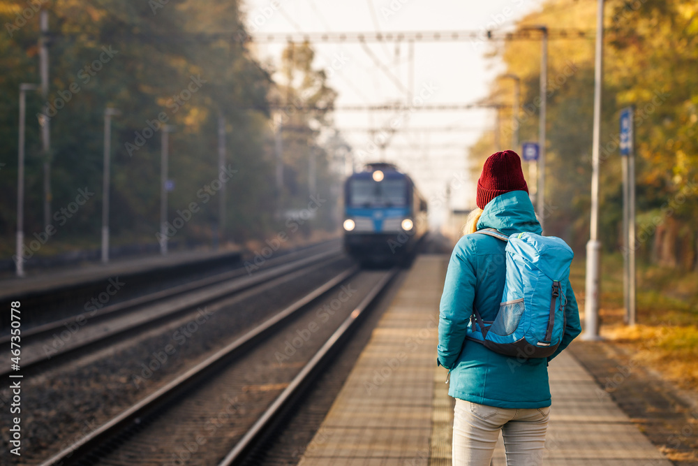 Woman with backpack is looking at arriving train at a railway station. Travel and transportation concept