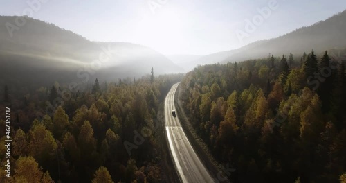 One gray silver crossover SUV car driving alone road trip, travel on freeway through dense colorful forest corridor at autumn sunny sunset - Aerial drone wide view