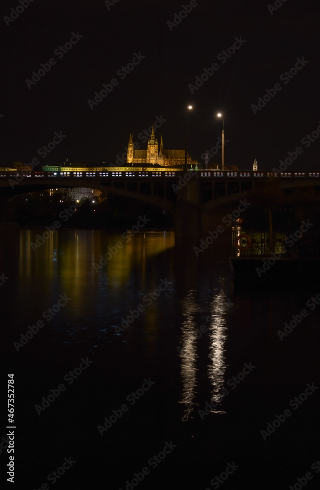 Night city with river and castle in the background, street lights are reflected in the water surface, beautiful urban landscape