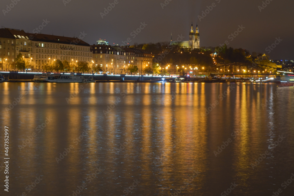 Night city with river, street lights are reflected in the water surface, in the background a historic building