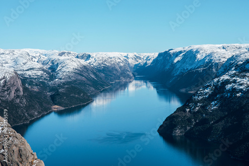 Scenic landscape of lake with the rocky shore with mountains with snowy peaks. Top view of the Pulpit Rock, Preikestolen