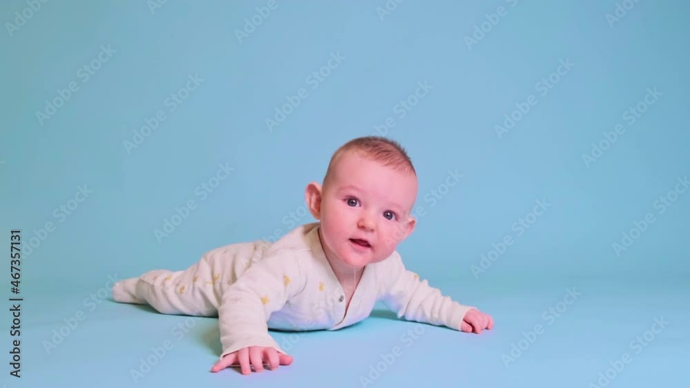 Happy infant baby boy laughing lying on his tummy, blue studio background. Four month old child close up Happy infant baby boy laughing lying on his tummy, blue studio background. Four month old child close up
