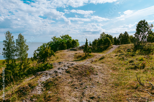 Uugu bluff or cliff on the Muhu Island in Estonia, located by the Baltic sea and near the island of Saaremaa. Beautiful sunny day with blue sky, white clouds, forest and stone cliffs by the seaside.