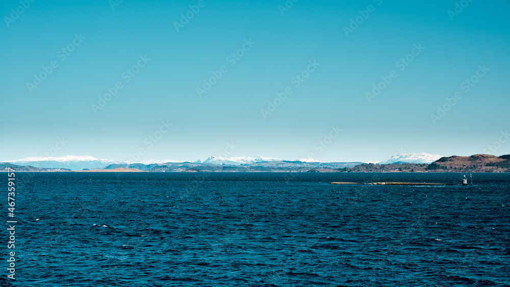 Scenic view of dark blue sea with stony island and mountains on background in Norway