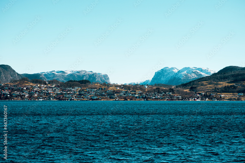 Beautiful scenic view of cold blue sea, island with small rorbu houses and mountains with snowy peaks on the background
