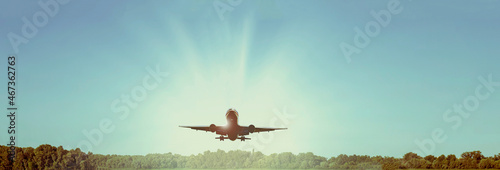 Passenger plane over the forest in the blue sky, the sun is shining. Transport, travel 
