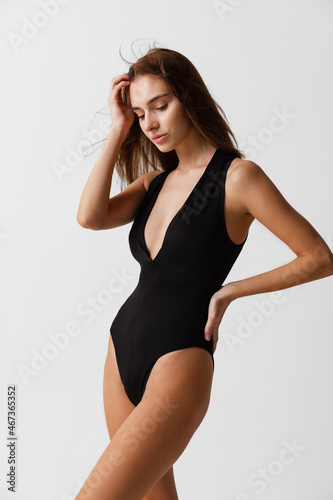 Portrait of young beautiful slim woman in black swimsuit posing isolated over gray studio background. Natural beauty concept. © master1305