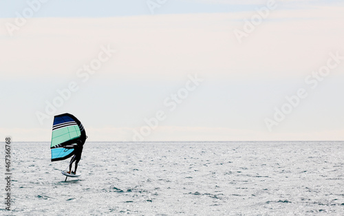 Man practicing wing foil with hydrofoil at sunset in the sea